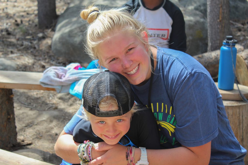Summer Camp counselor smiles at camera while hugging camper