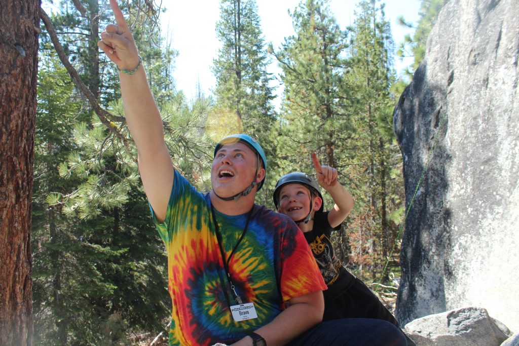Summer Camp staff member at Gold Arrow Camp in a tie dye shirt points at the sky while a young boy points along with him